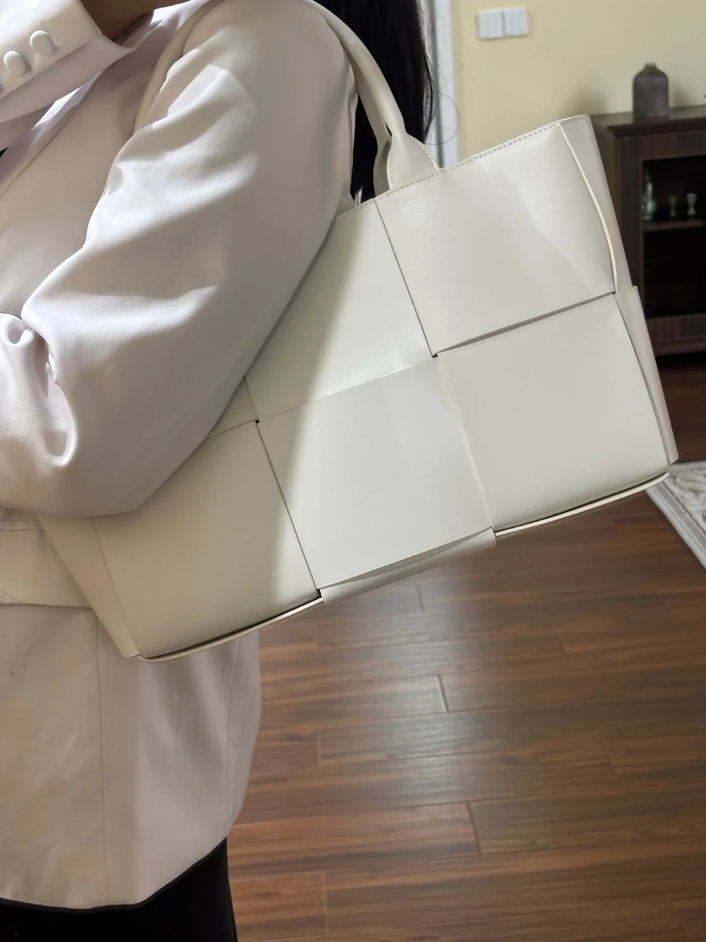 Woman carrying a large white quilted leather tote bag with woven texture and top handles.