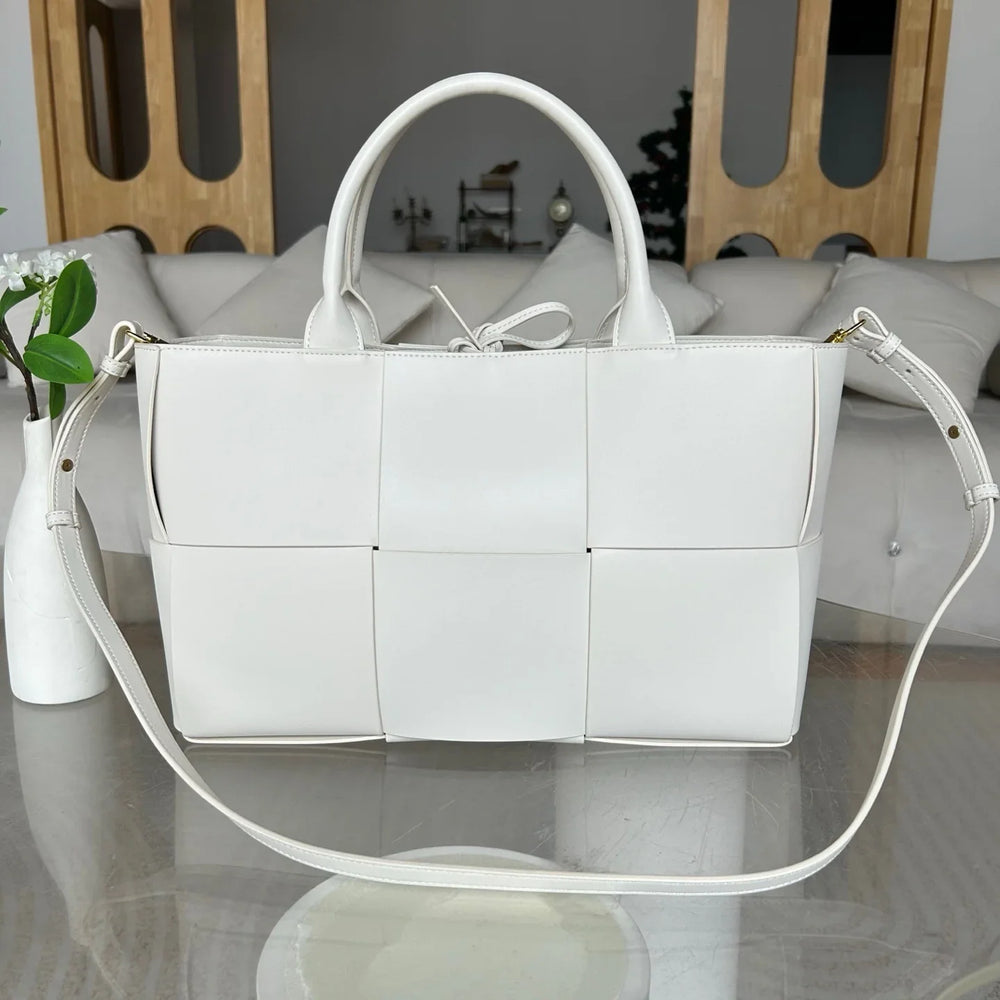 Large white woven leather tote bag with top handles and adjustable shoulder strap on a table