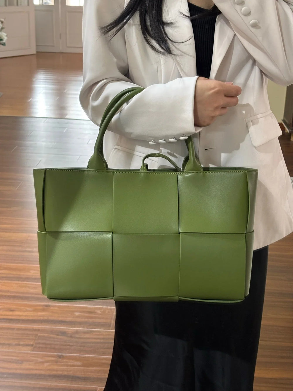 Woman holding large green quilted leather tote bag with top handles, minimalist style