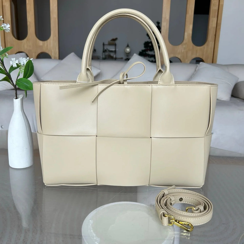 Beige woven leather tote bag with top handles and detachable shoulder strap on table
