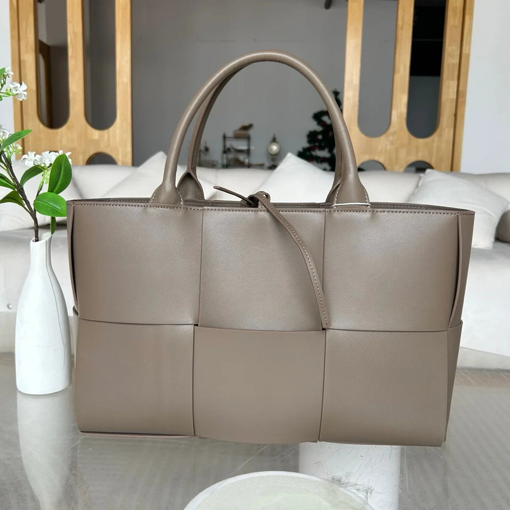 Taupe quilted large leather tote bag with top handles on a glass table, minimalist interior