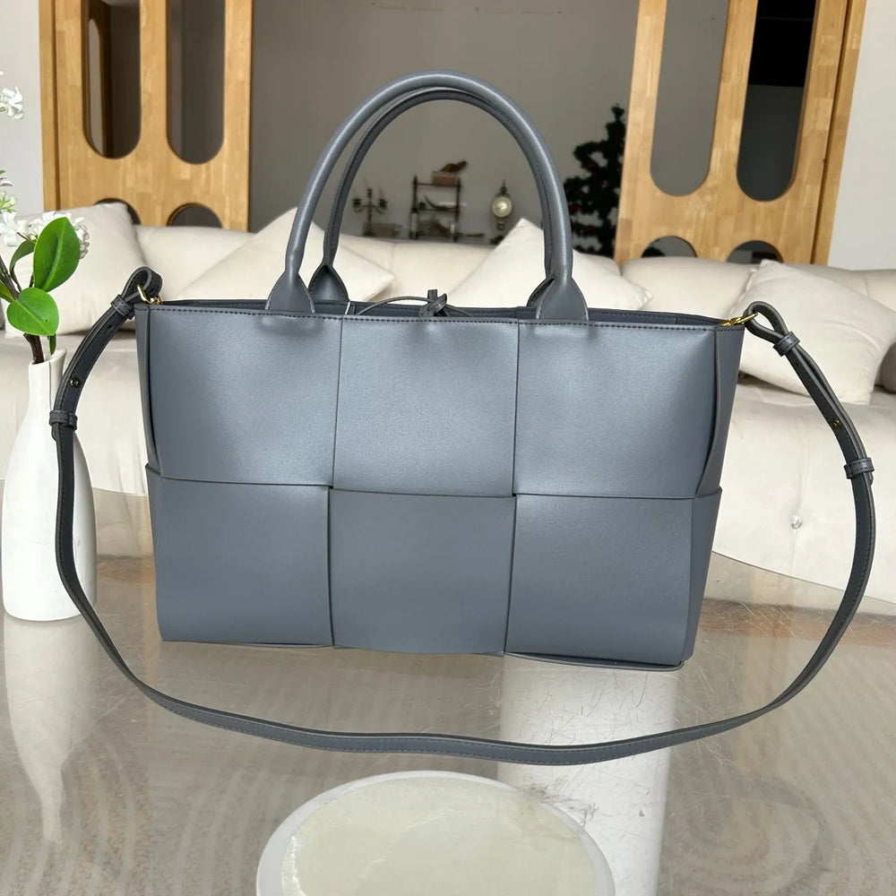 Quilted large gray leather tote bag with top handles and adjustable shoulder strap on glass table