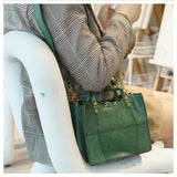 Green full grain leather small handbag with top handles and gold hardware, worn crossbody.