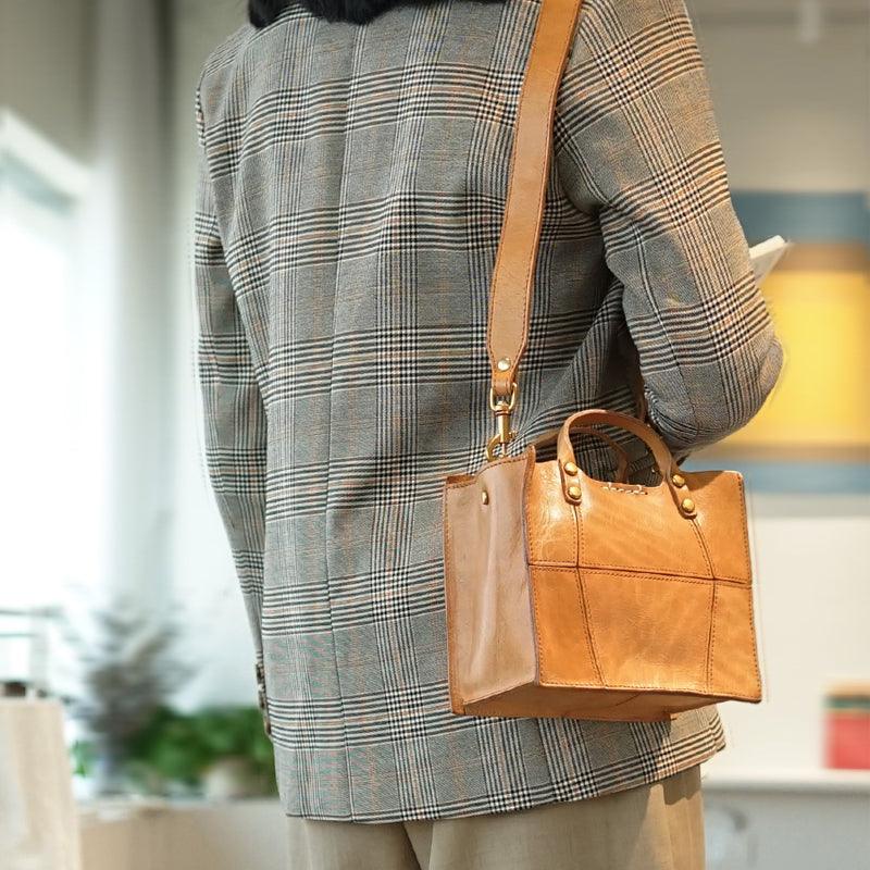 Tan full grain leather small shoulder bag with top handle worn crossbody by a person in a plaid blazer