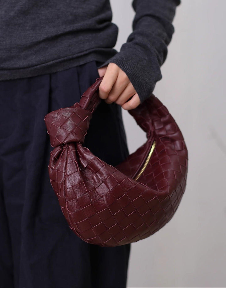 Hand holding a small burgundy lambskin knotted intrecciato leather handbag with zipper
