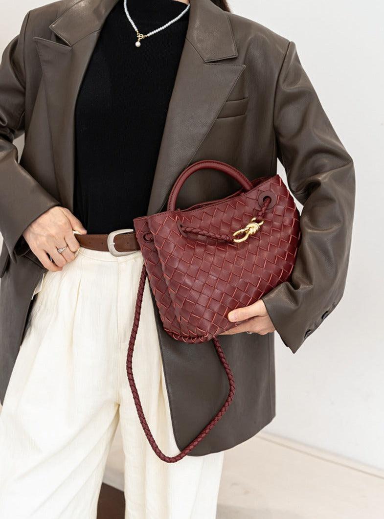 Woven lambskin leather shoulder bag with gold buckle and braided strap, held by woman in brown blazer.