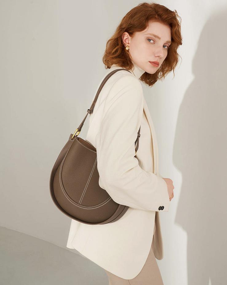 Woman in cream blazer with brown smooth calfskin leather saddle bag shoulder purse