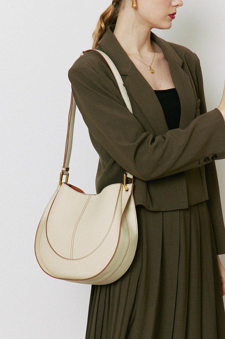 Woman wearing a beige smooth calfskin leather saddle bag with gold hardware on shoulder