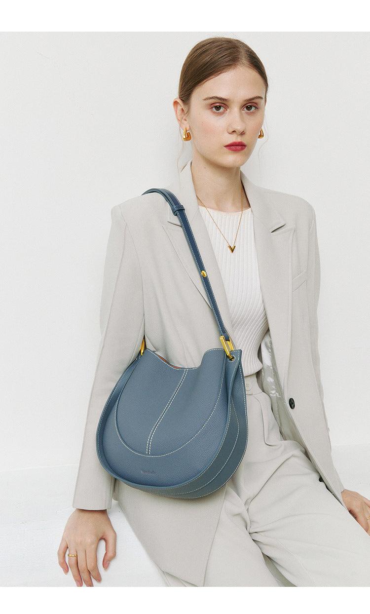 Woman in a light suit with a blue smooth calfskin leather saddle bag and gold hardware.