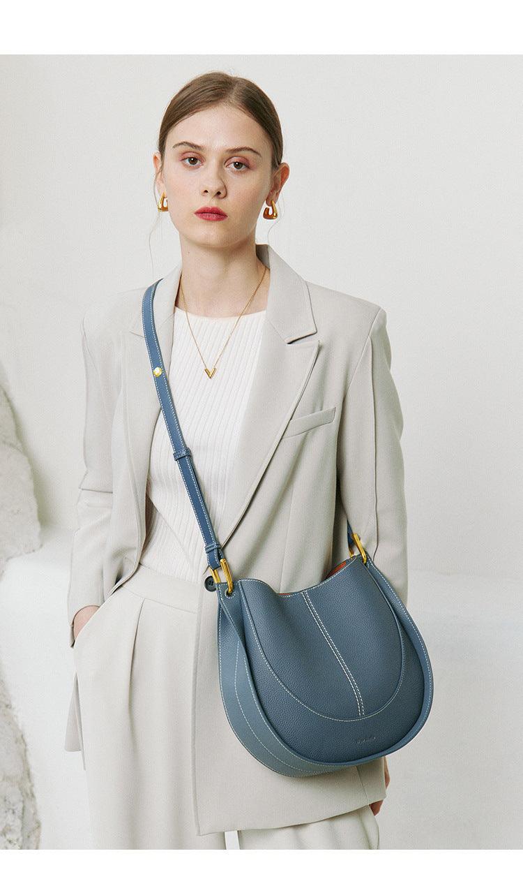 Woman in a cream suit with a blue smooth calfskin leather saddle bag crossbody