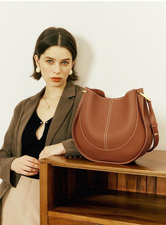 Woman posing with a brown smooth calfskin leather saddle bag on a wooden shelf