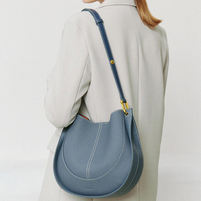 Woman wearing a light coat with a blue smooth calfskin leather saddle bag with white stitching