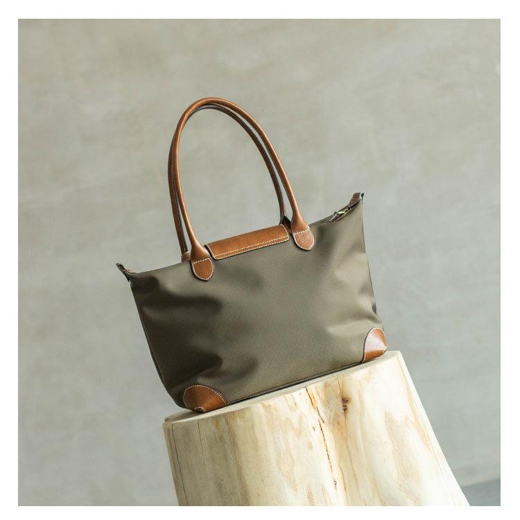 Olive nylon tote bag with brown leather handles and trim, displayed on a wooden stand.