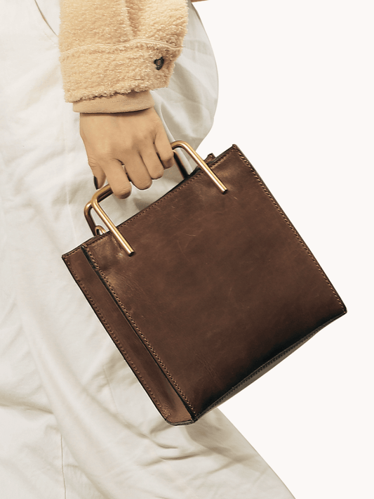 Woman holding a brown leather handbag with gold handles, stylish and minimalist design