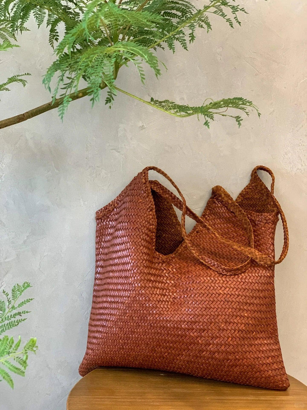 Brown woven leather hobo tote bag with braided handles on a wooden table, indoor setting