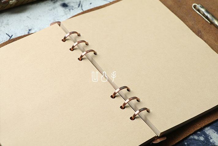 A6 vintage leather sketchbook with blank kraft paper and copper rings, open on a desk.