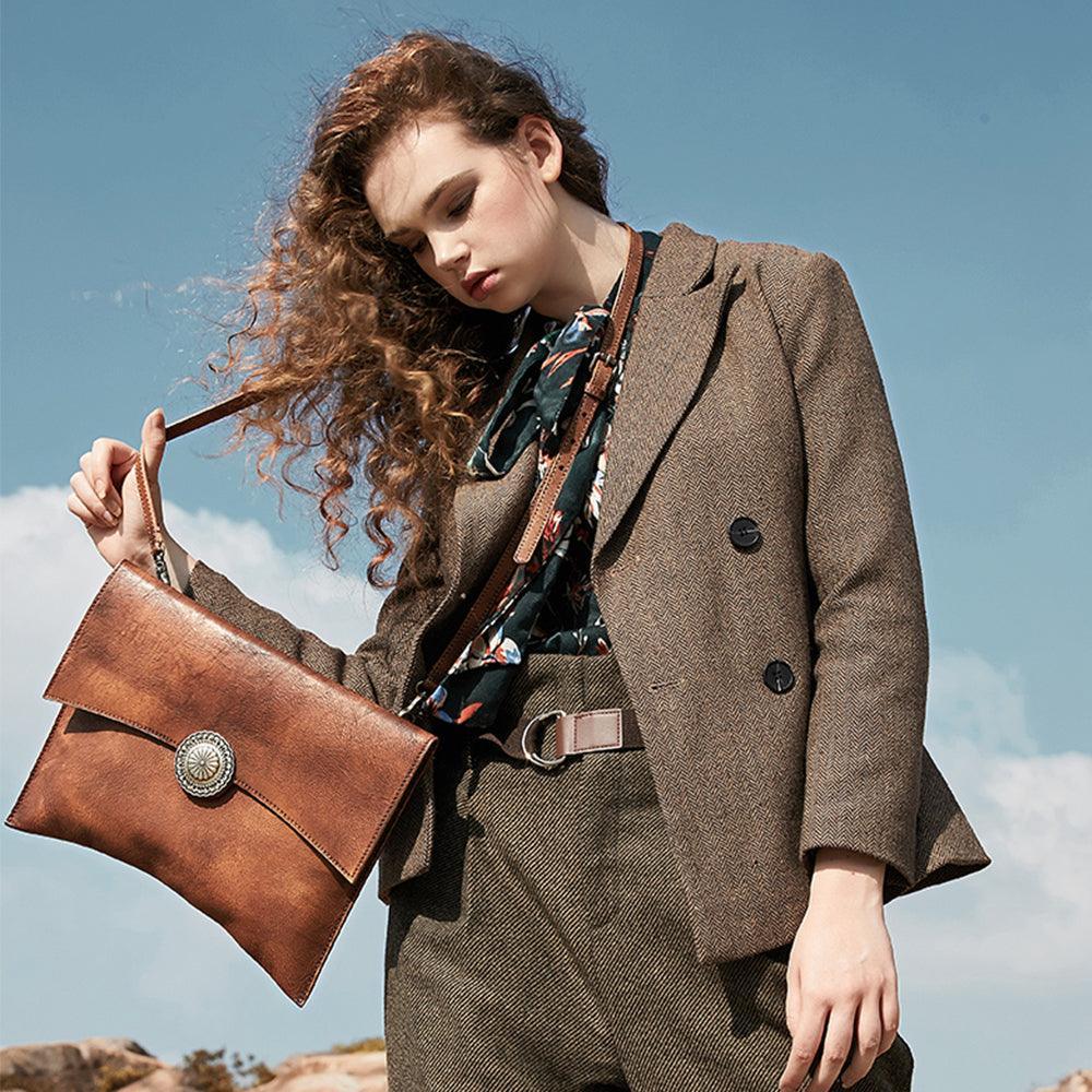 Woman outdoors holding large handcrafted brown leather clutch shoulder bag with decorative clasp