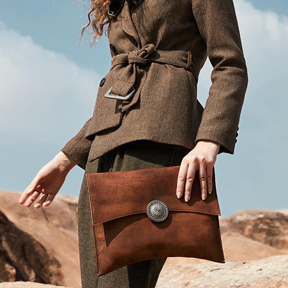 Woman holding a large handcrafted brown leather clutch bag with metal accent outdoors