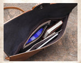 Interior of brown handcrafted leather clutch bag with organized pockets holding a tablet, book, and pouch