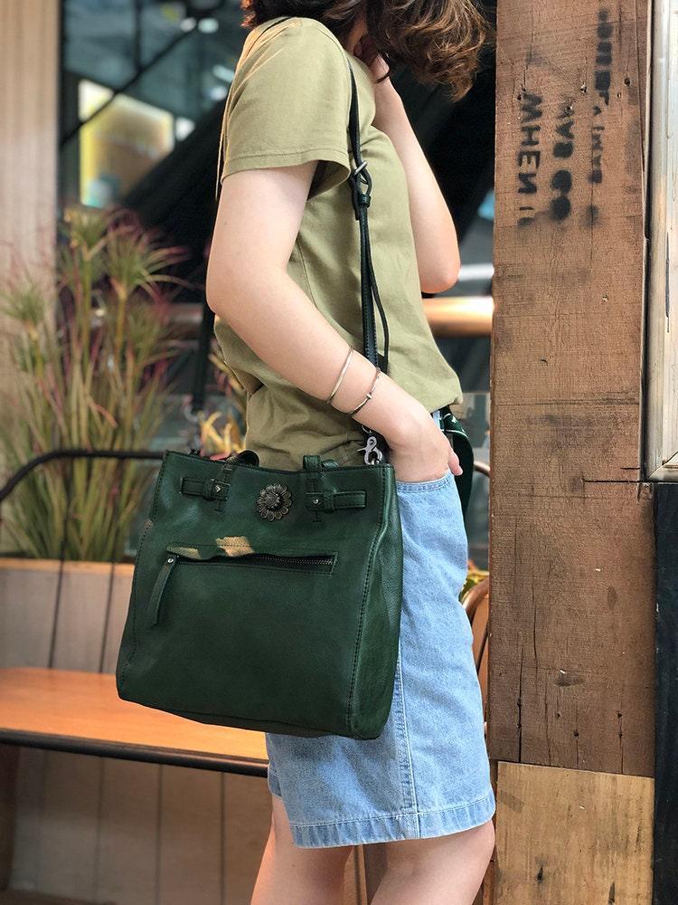 Woman wearing a green leather cowhide shoulder bag with front zipper and floral detail