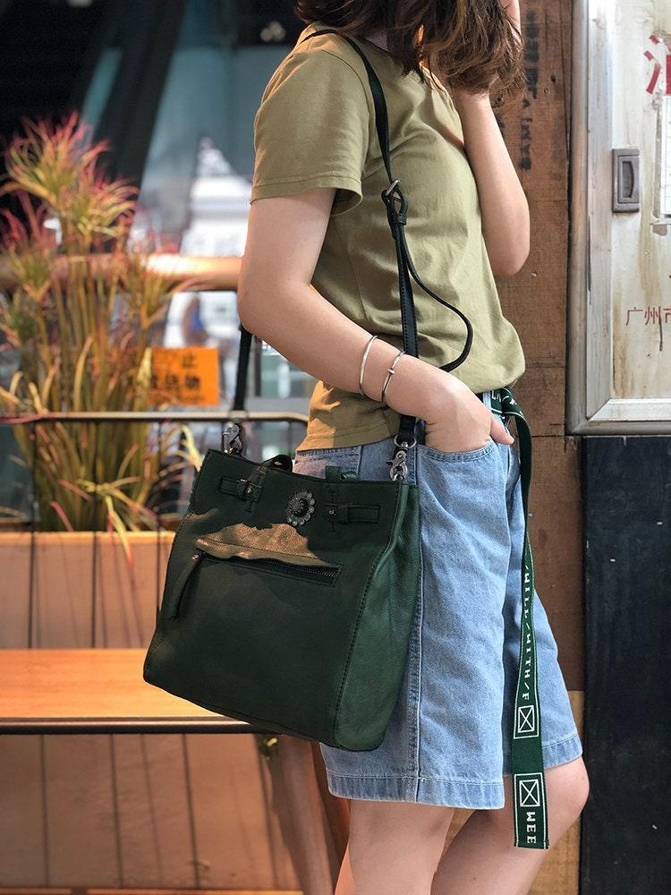 Woman carrying a large green leather shoulder bag with zipper detail, casual street style