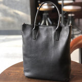 Black full grain leather tote bag with handles on wooden table in cafe setting