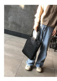 Woman holding large black full grain leather tote bag, casual outfit, concrete background