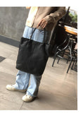 Woman holding a large black full grain leather tote bag, casual outfit, indoor setting
