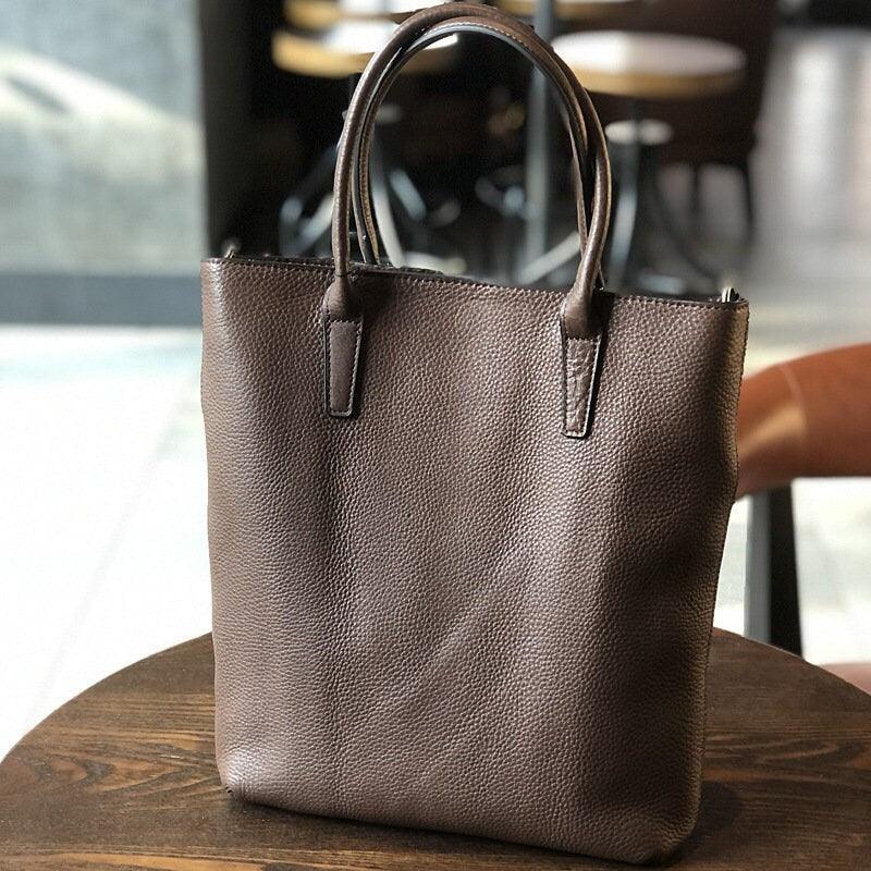 Full grain brown leather tote bag with double handles on a wooden table in a café setting