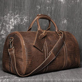 Brown full-grain leather duffle bag with crocodile pattern and shoulder strap on textured background