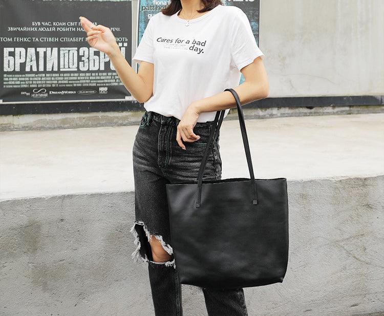 Woman holding large black full grain leather tote bag, casual outfit, outdoor setting