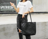 Woman holding large black full grain leather tote bag, casual outfit, outdoor setting