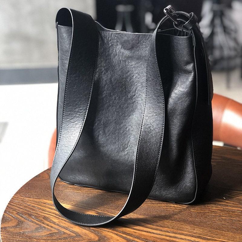Full grain black leather shoulder bag with wide strap on a wooden table