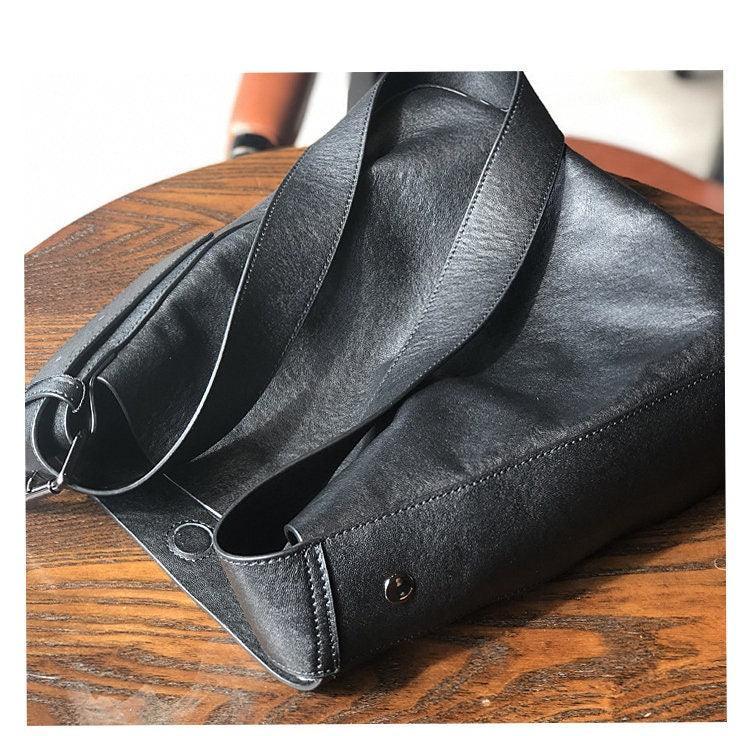 Black full grain leather shoulder bag with wide strap on wooden table