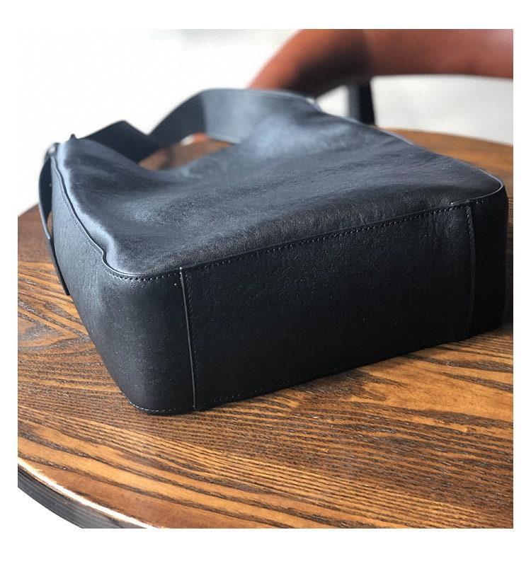 Black full grain leather shoulder bag with wide strap on wooden table