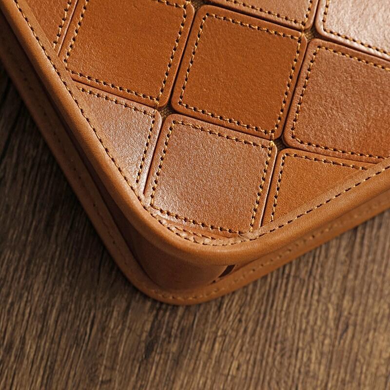 Close-up of tan cowhide leather handbag with stitched geometric pattern on wooden surface