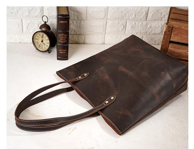 Large handcrafted dark brown leather tote bag with double handles on a white table.