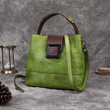 Handcrafted green leather shoulder bag with brown strap and crossbody feature on grey background