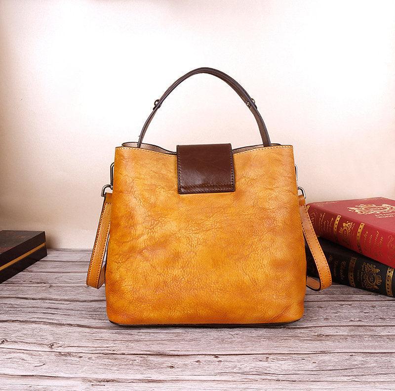 Handcrafted tan leather shoulder bag with dark brown handle and clasp on wood surface