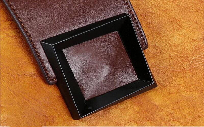 Close-up of a handcrafted brown leather handbag with black square buckle on tanned leather surface