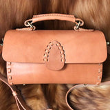 Handcrafted tan leather shoulder bag with stitched detailing and top handle on fur background