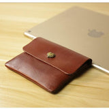 Handcrafted brown leather slim wallet with gold button on wooden table beside tablet