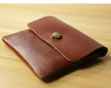 Handcrafted brown leather slim wallet with heart-shaped clasp on wooden surface