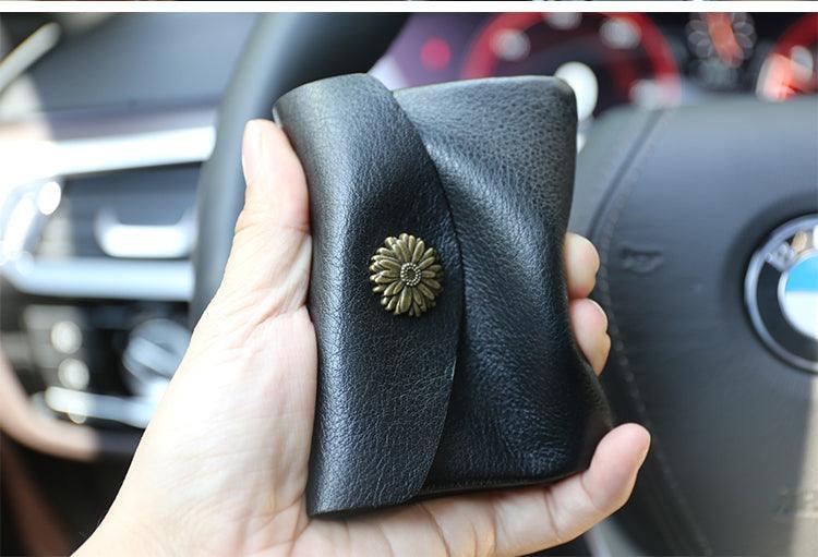 Hand holding a black handcrafted leather slim wallet with floral metal button, in car interior