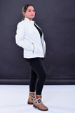 Woman wearing white genuine leather biker jacket with zipper pockets, black pants, and tan patterned boots, posing against dark background.
