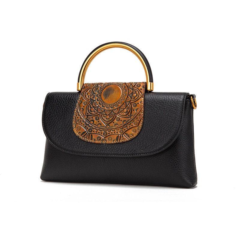 Black leather handbag with gold metal handle and embossed brown flap design
