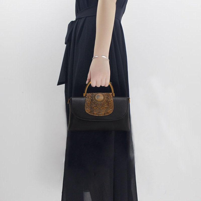 Woman in black dress holding black leather handbag with embossed brown flap and top handle