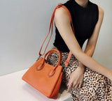 Woman holding orange leather handbag with top handles and shoulder strap, animal print skirt