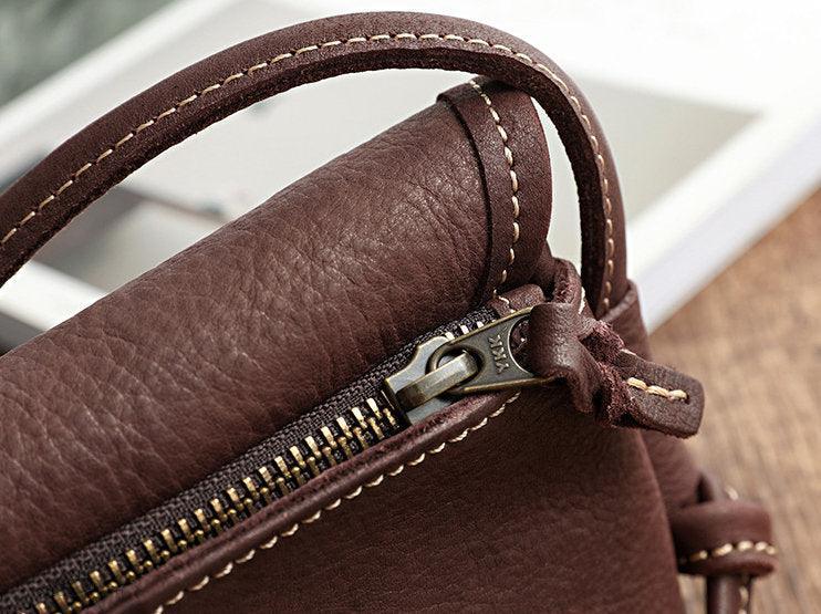 Close-up of brown cowhide leather shoulder bag with visible stitching and zipper detail