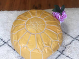 Handmade light yellow Moroccan leather pouf footstool on a textured rug, vase with pink flowers nearby